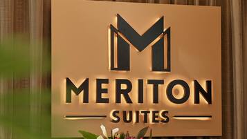 A reception desk with a sign for Meriton Suites, a potted plant, and a Dell computer.