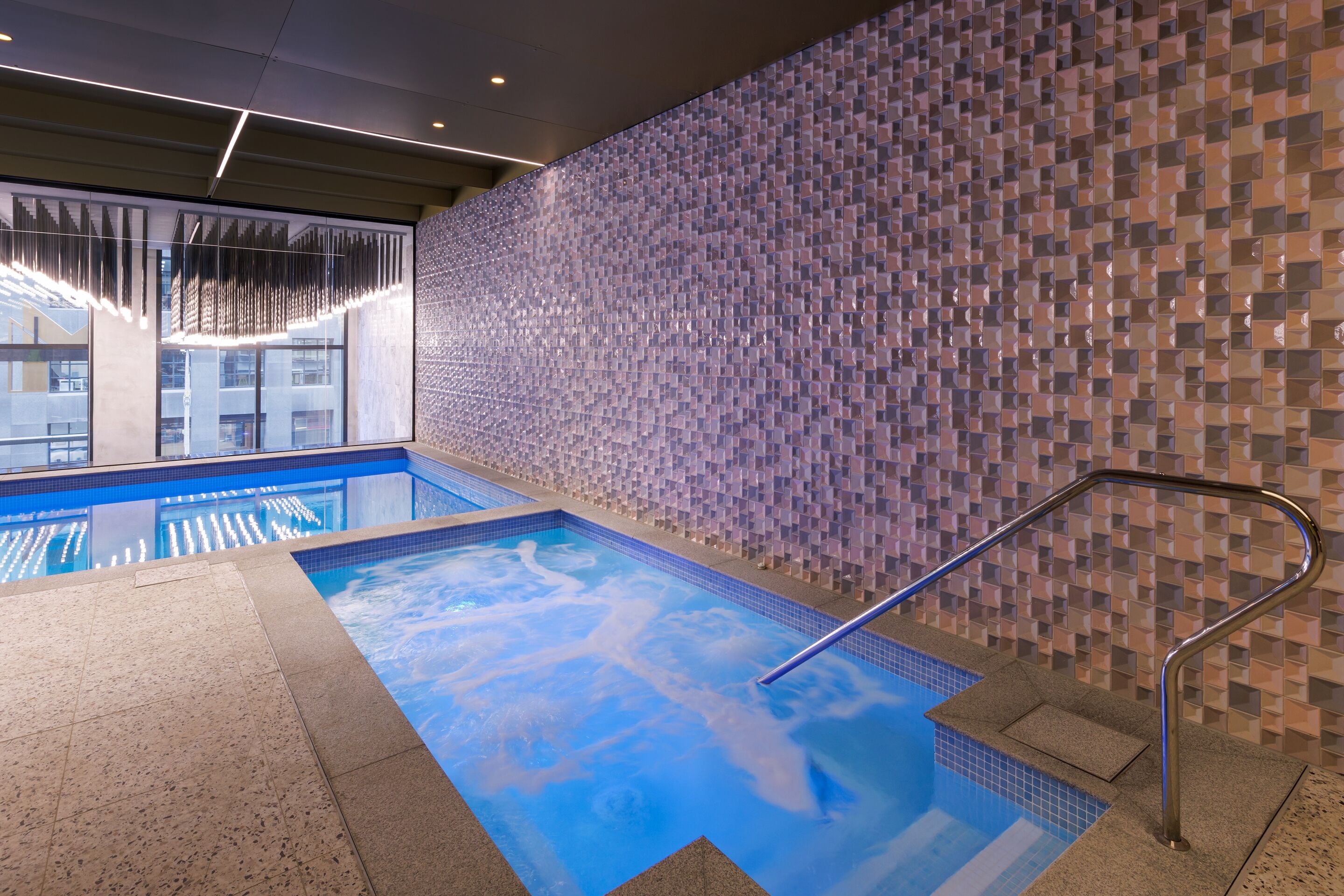 Una piscina interior con pared de azulejos y barandilla de metal.