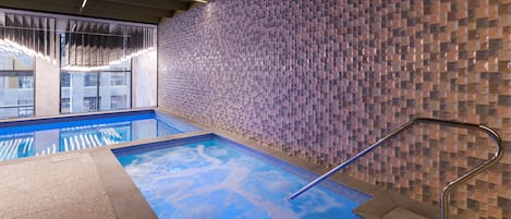 Una piscina interior con pared de azulejos y barandilla de metal.