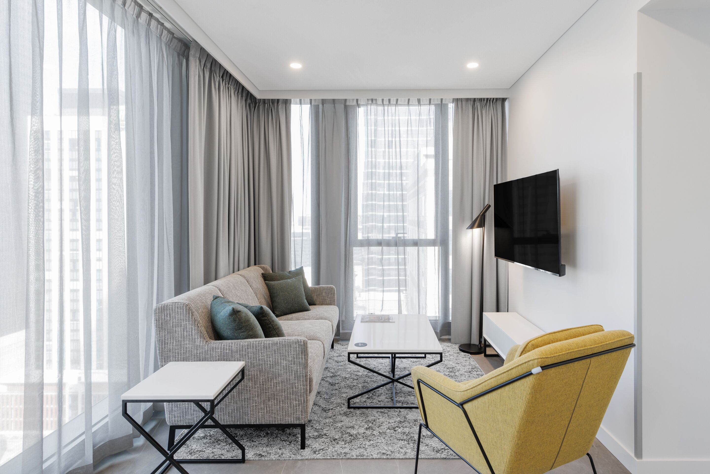 A modern living room with a sofa, a yellow armchair, a coffee table, and a TV mounted on the wall.