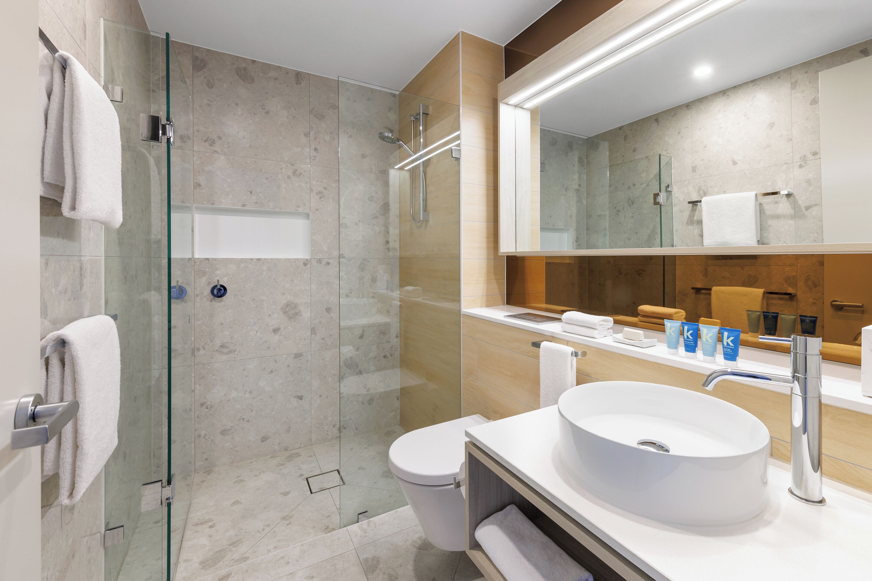 Ein modernes Badezimmer mit einer gläsernen Dusche, einem weißen Waschbecken und einem großen Spiegel.