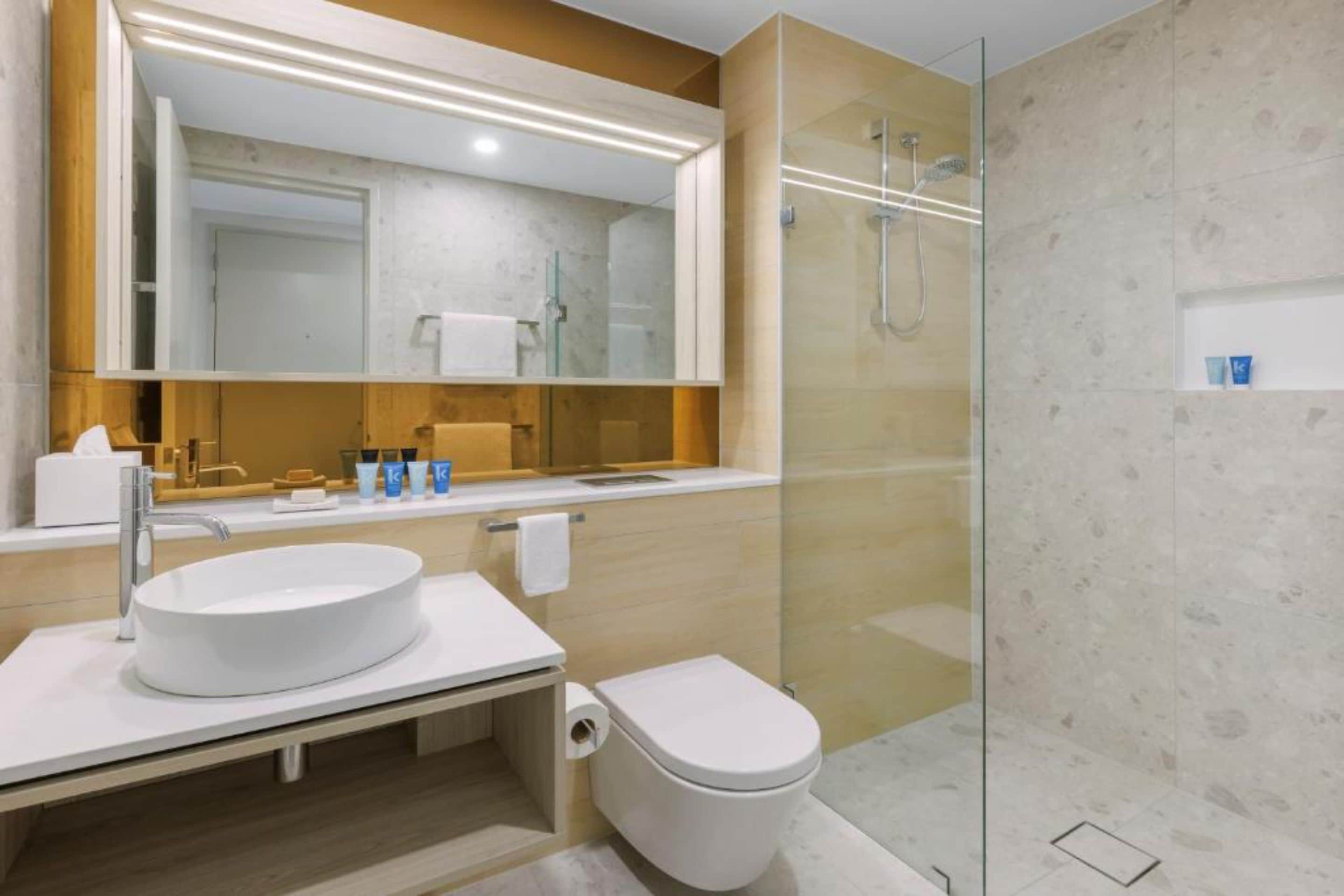 Un baño moderno con un lavabo redondo, un inodoro y una zona de ducha con mampara de vidrio.