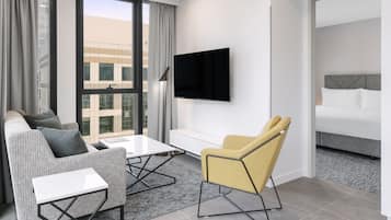 Et moderne hotelværelse med sofa, lænestol i gult, fladskærms-TV og seng.