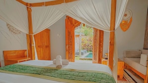Una habitación con una cama grande, cabecera de madera y dosel. Hay una pequeña mesa y un banco en la esquina.