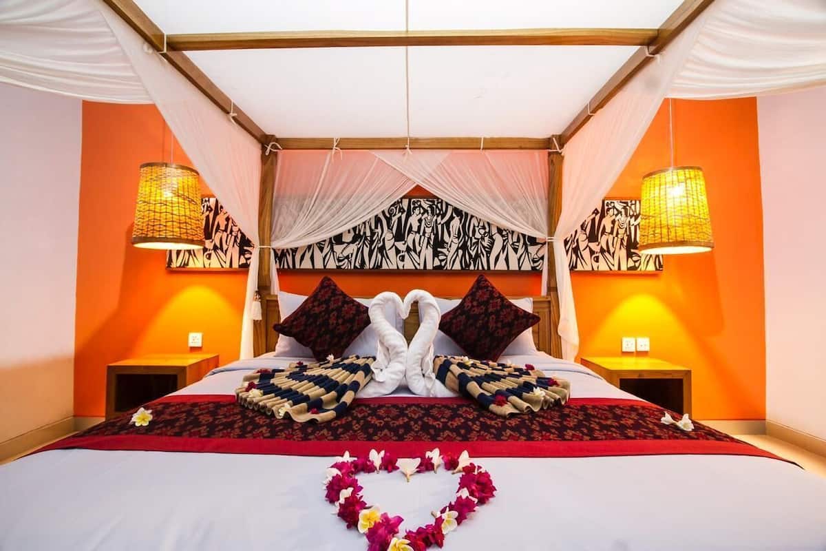 A bed with a canopy, two bedside lamps, and a decorative wall painting.