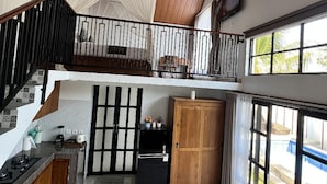 Et rummeligt køkken med et moderne design, komplet med et marmorgulv, træskabe og et sort køleskab. Der er en balkon med gelænder og udsigt over naturen.