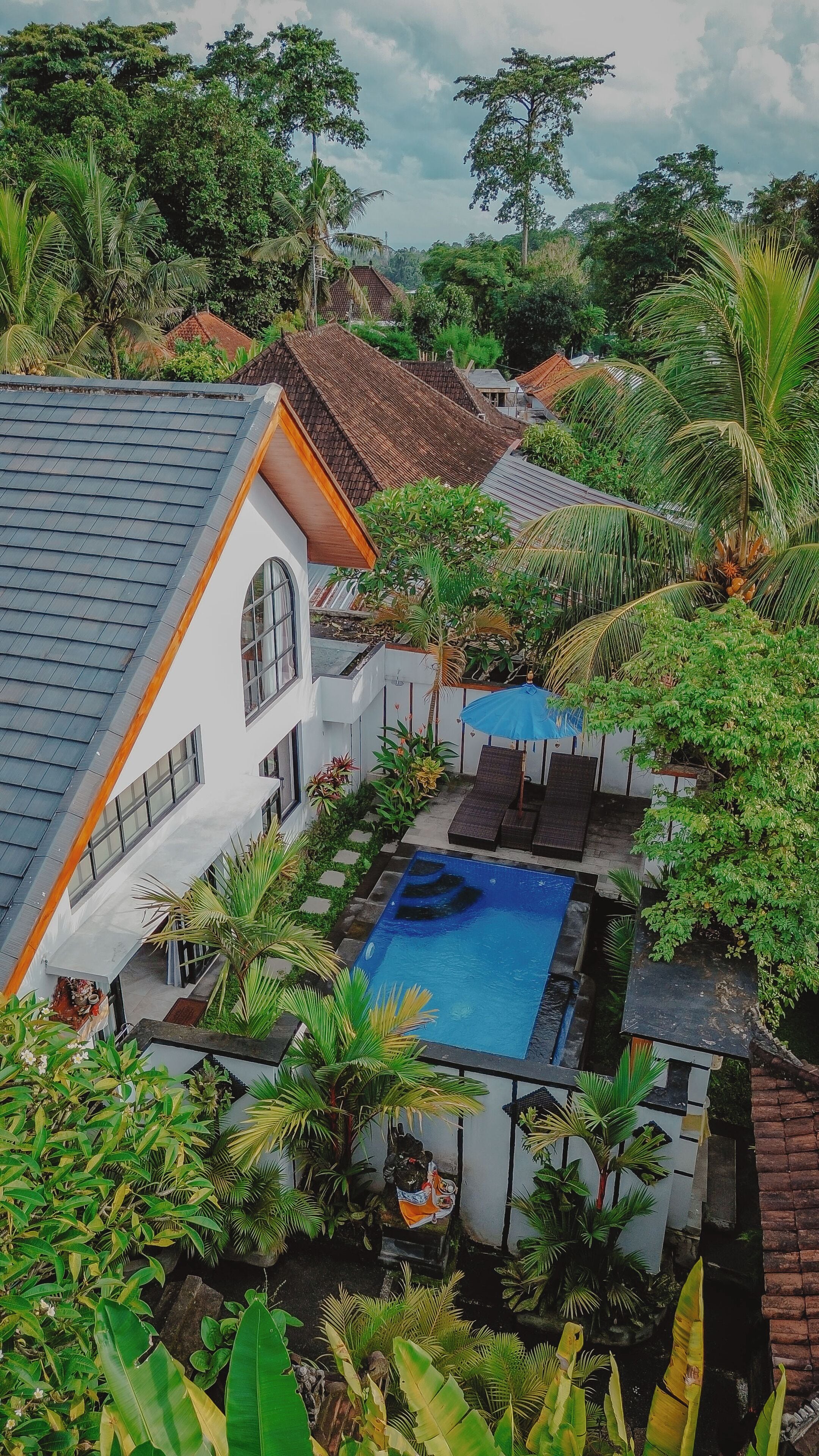 A residential area with a swimming pool surrounded by lush greenery and a white building with a tiled roof.