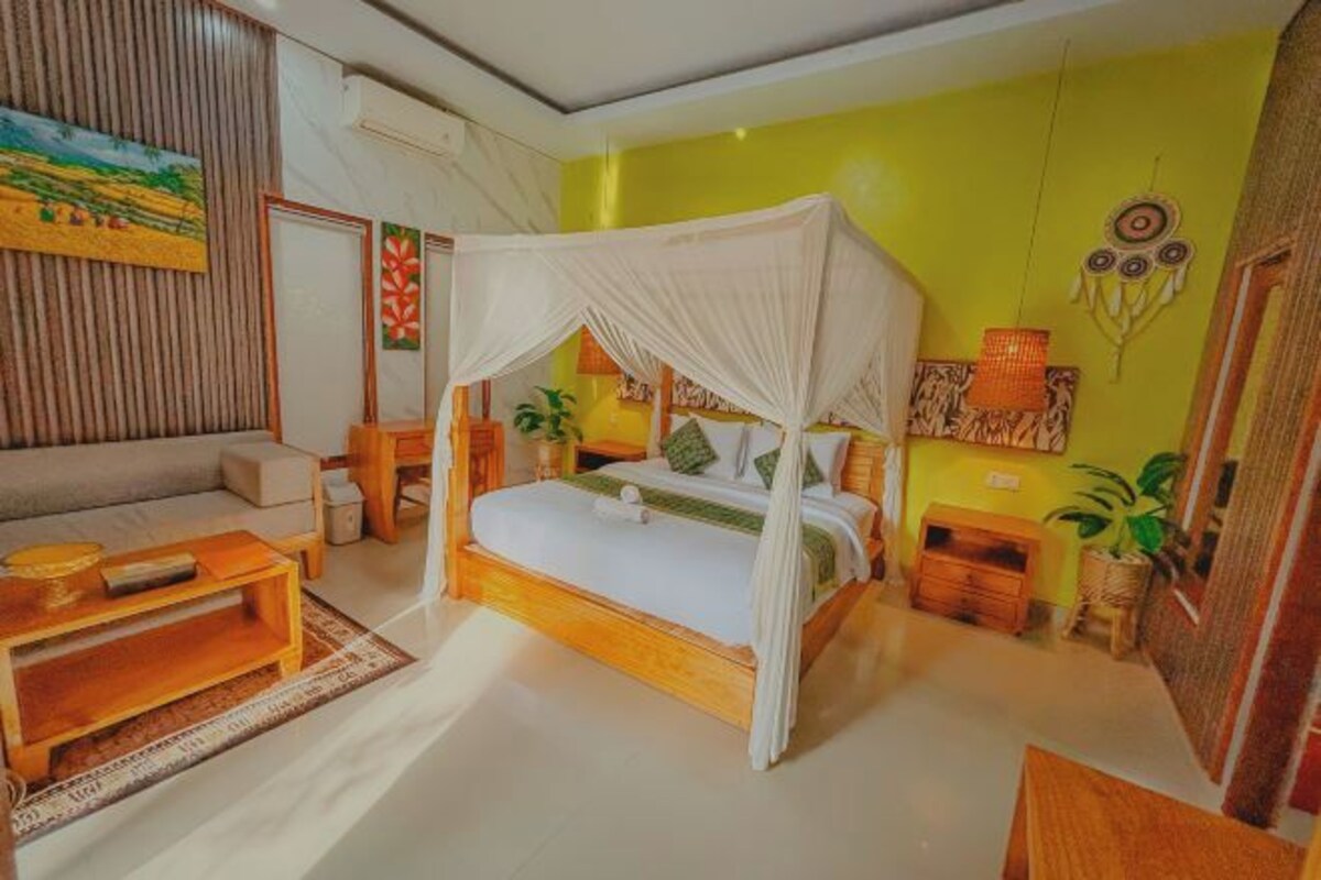 A bedroom with a canopy bed, a sofa, a wooden coffee table, and a small table with a lamp.