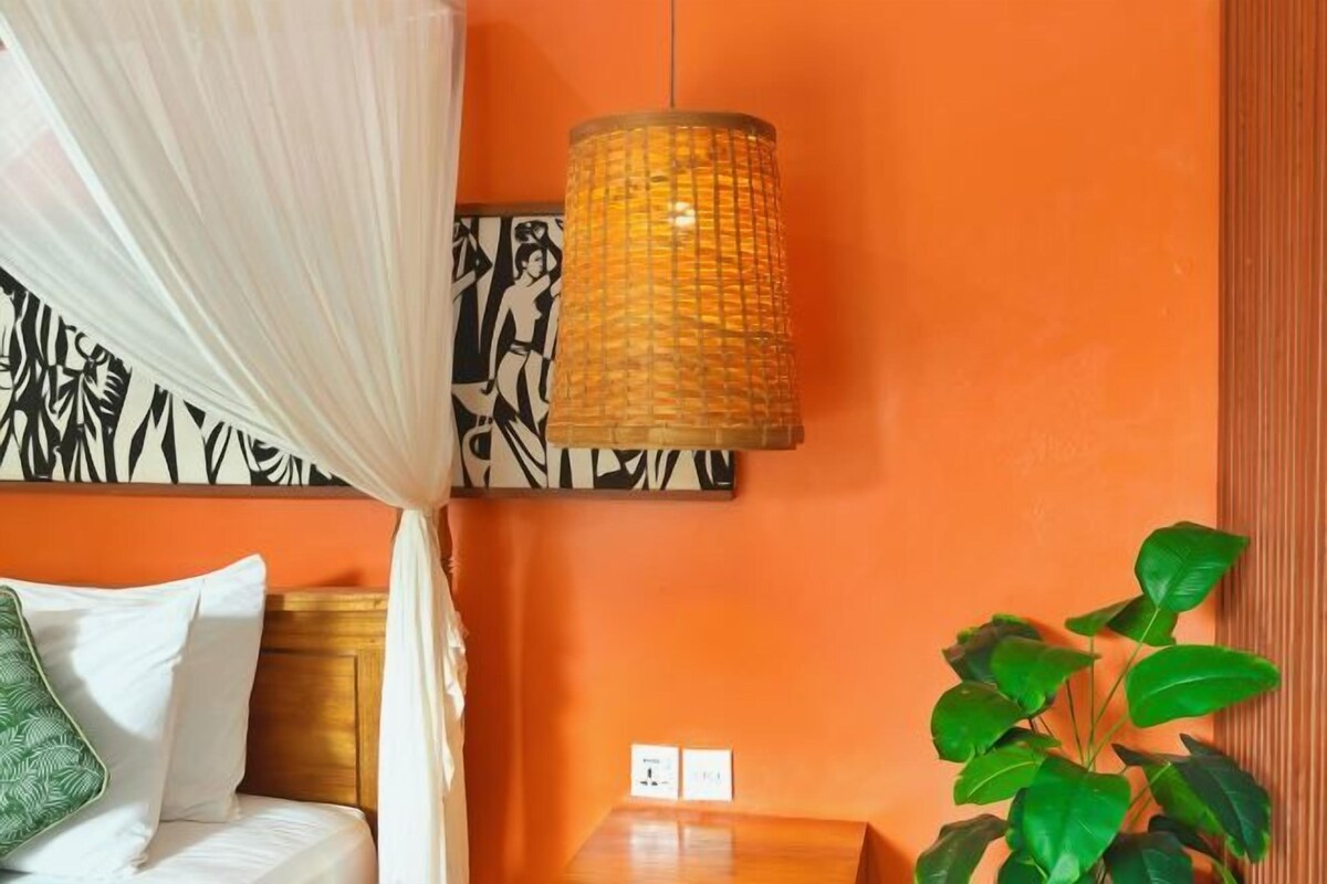 A room with a bed, a hanging lamp, a wall with a black and white pattern, and a green plant.