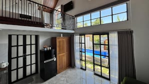 Amplia sala de estar con balcón, ventanas grandes y vista a una piscina.