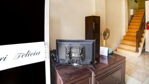 Una habitación con una televisión sobre un mueble de madera, un calendario y un ventilador.