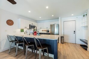Une cuisine moderne avec des meubles blancs, des appareils en acier inoxydable et un îlot central doté de tabourets de bar.