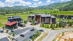 A modern hotel with multiple floors, a parking lot, and a view of surrounding mountains.