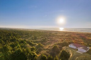 A house with a red roof, surrounded by dense greenery and a beach in the background. - Vista Del Mare Beach House (Ocean Shores)