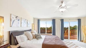 A bedroom with a large bed, a ceiling fan, and a balcony with a wooden deck.