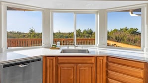 A kitchen with a large island, wooden cabinets, and a view of a wooden deck and greenery.