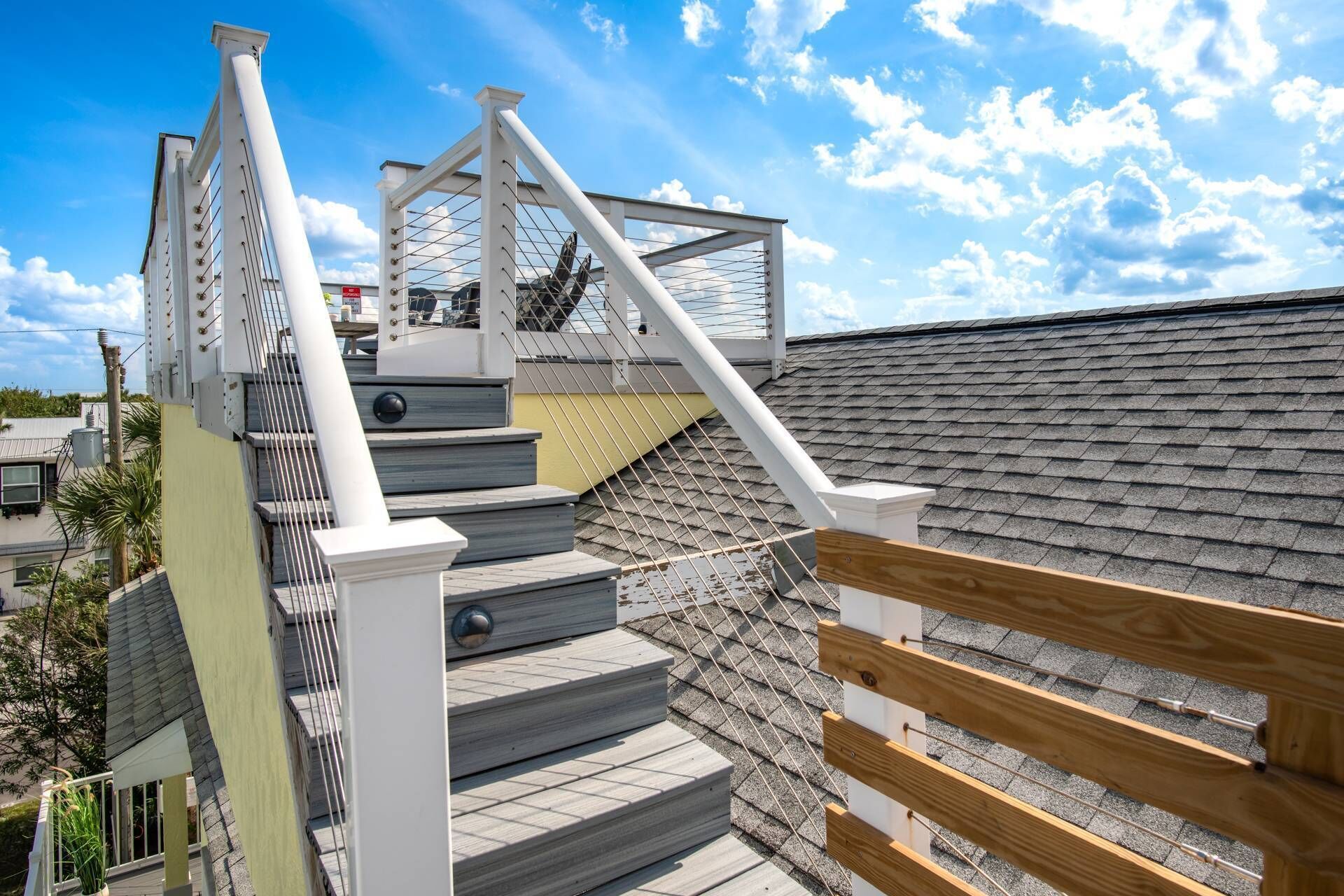 Un toit-terrasse aménagé en espace de vie, avec un escalier menant à une terrasse, le tout entouré d’une rambarde en métal et d’une clôture en bois.