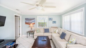 A living room with a beige sofa, a wooden coffee table, a ceiling fan, and a television on a stand.
