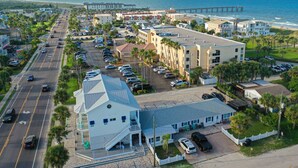 A coastal hotel with a parking lot, multiple buildings, and a pier in the background.