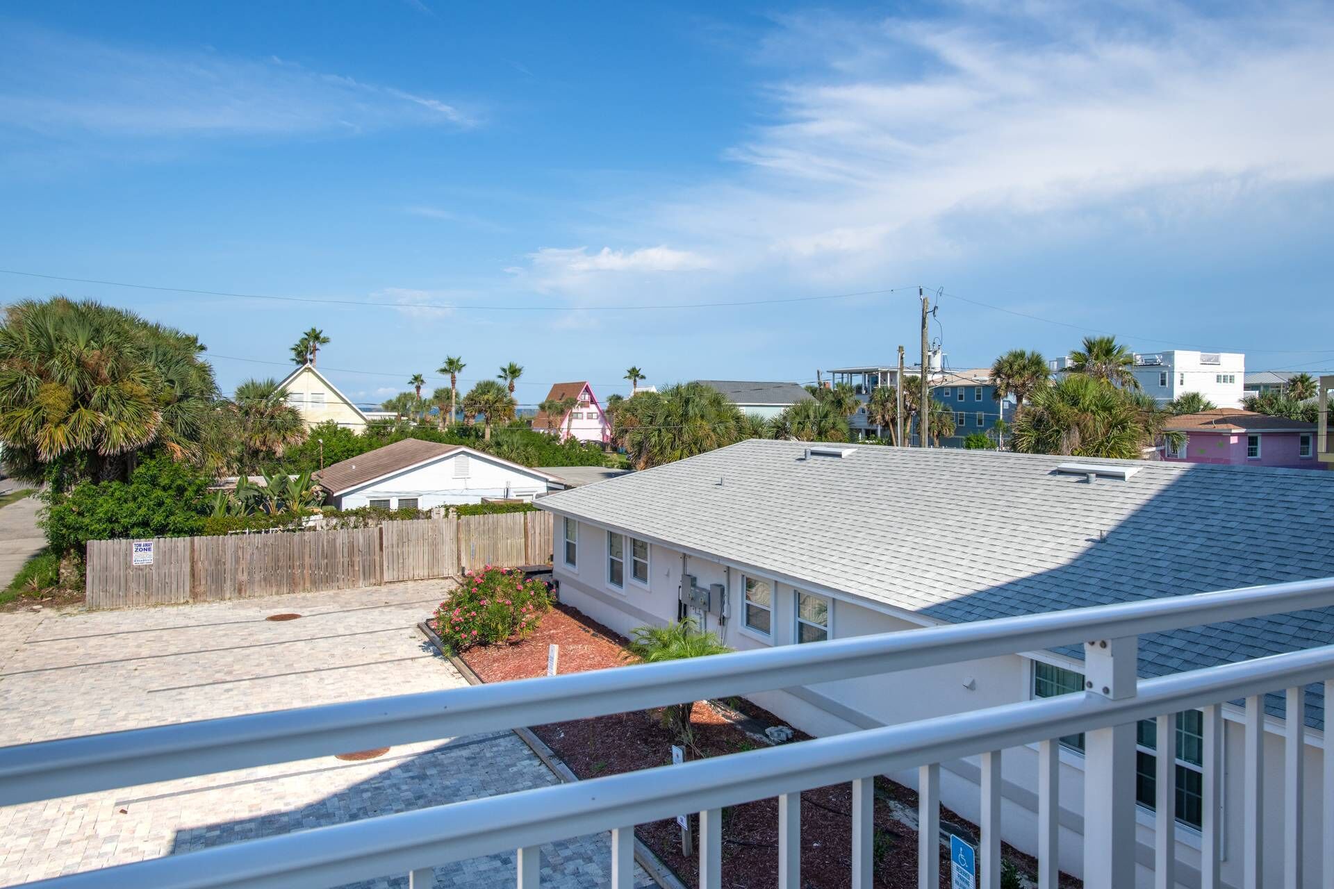 A residential area with a white house, a wooden fence, and a clear blue sky.