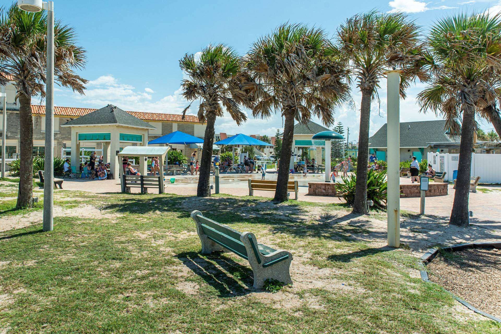 A sunny outdoor area with palm trees, benches, and umbrellas.