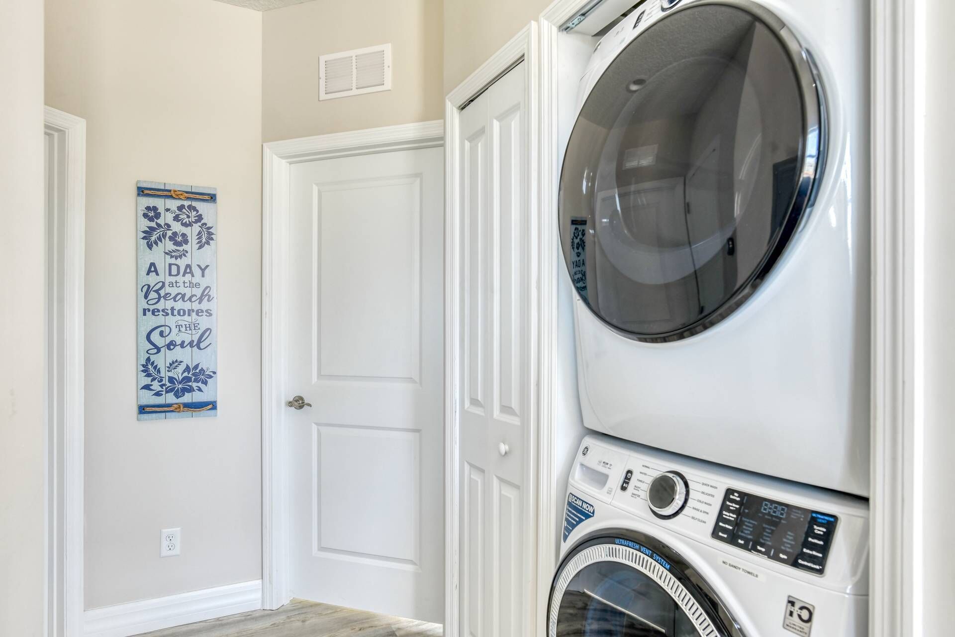 A laundry room with stacked washers and dryers, a door, and a poster on the wall.