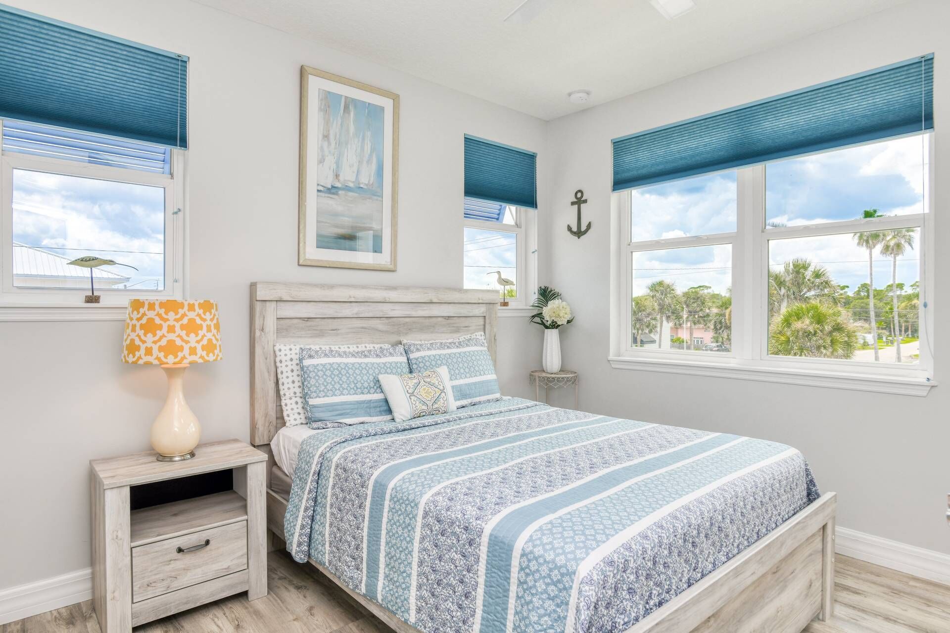 Un dormitorio con una cama, una mesita de noche, una lámpara y dos ventanas con persianas azules.