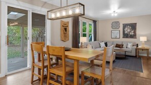 A dining area with a wooden table and chairs, a hanging light fixture, and a view through glass doors to an outdoor area.