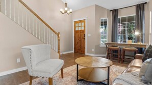 A living room with a staircase, a round wooden table, a sofa, and a window with curtains.