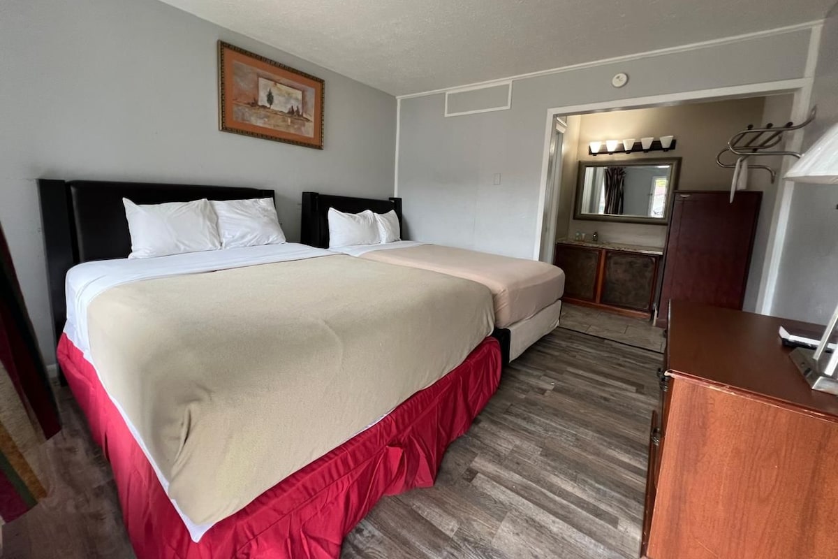 A hotel room with a large bed, a small kitchenette, and a wooden cabinet.