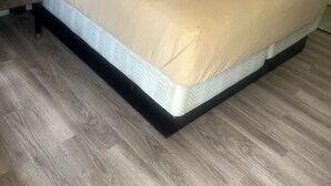 Een keurig opgemaakt bed met hoofdbord, een houten vloer en een effen muur.