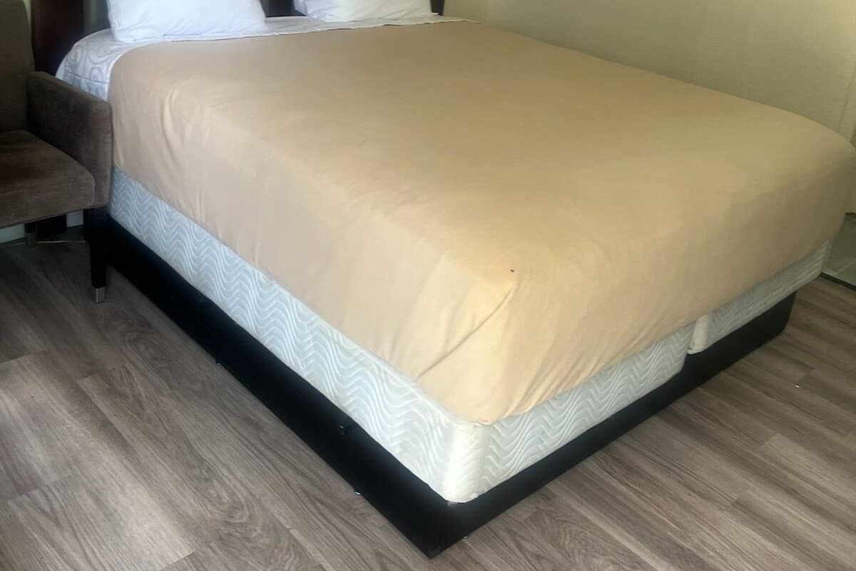 Ein ordentlich bezogenes Bett mit Kopfteil, Holzboden und schlichter Wand.