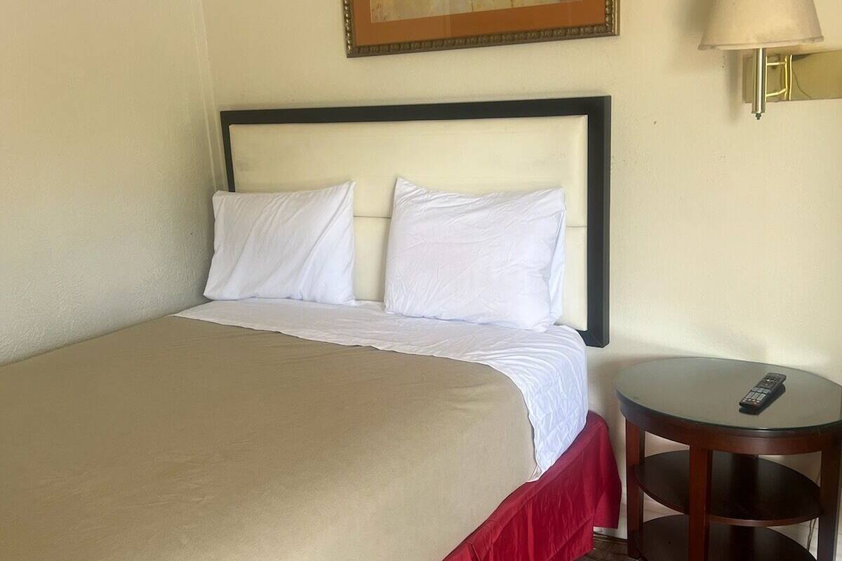 Ein Hotelzimmer mit einem großen Bett, einem Bild an der Wand, einer Nachttischlampe und einem kleinen Tisch mit einer Fernbedienung.