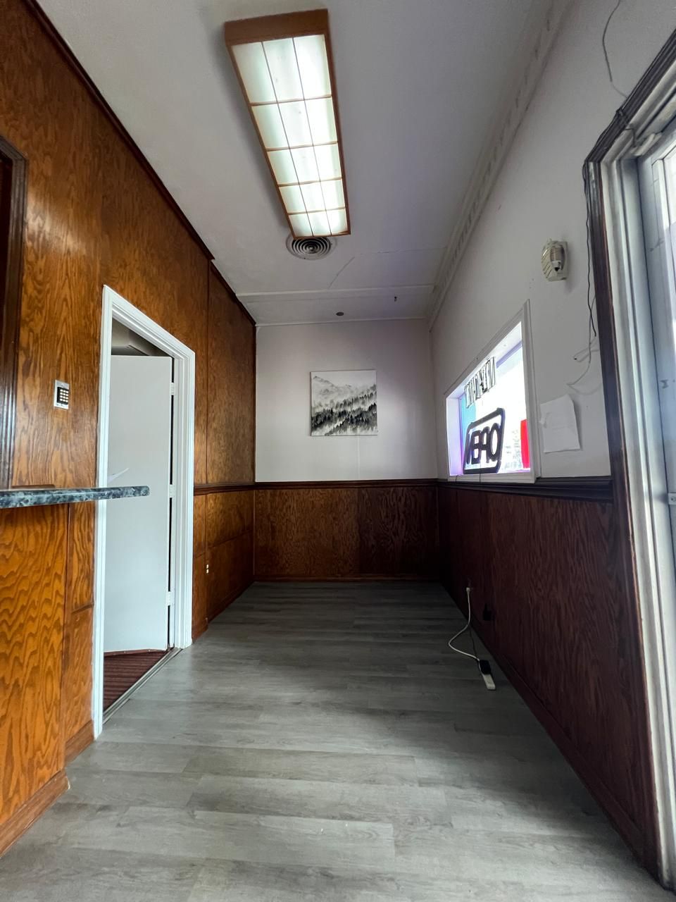Um corredor com painéis de madeira, luminária no teto, uma porta e ar-condicionado fixado na parede.
