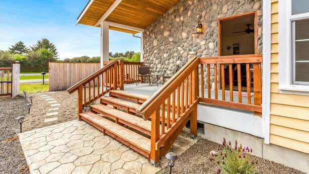 A stone exterior with a wooden deck and steps leading to a covered porch.