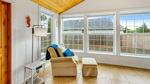 A spacious room with a wooden ceiling, large windows, a beige sofa, a small table, and a view of a backyard with a wooden fence.