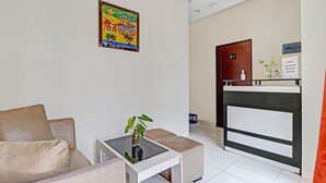 A hotel lobby with a beige sofa, a small table with a plant, a colorful painting, a reception desk, and a door labeled "01". - OYO 90452 Pillow Inn (Karawang)