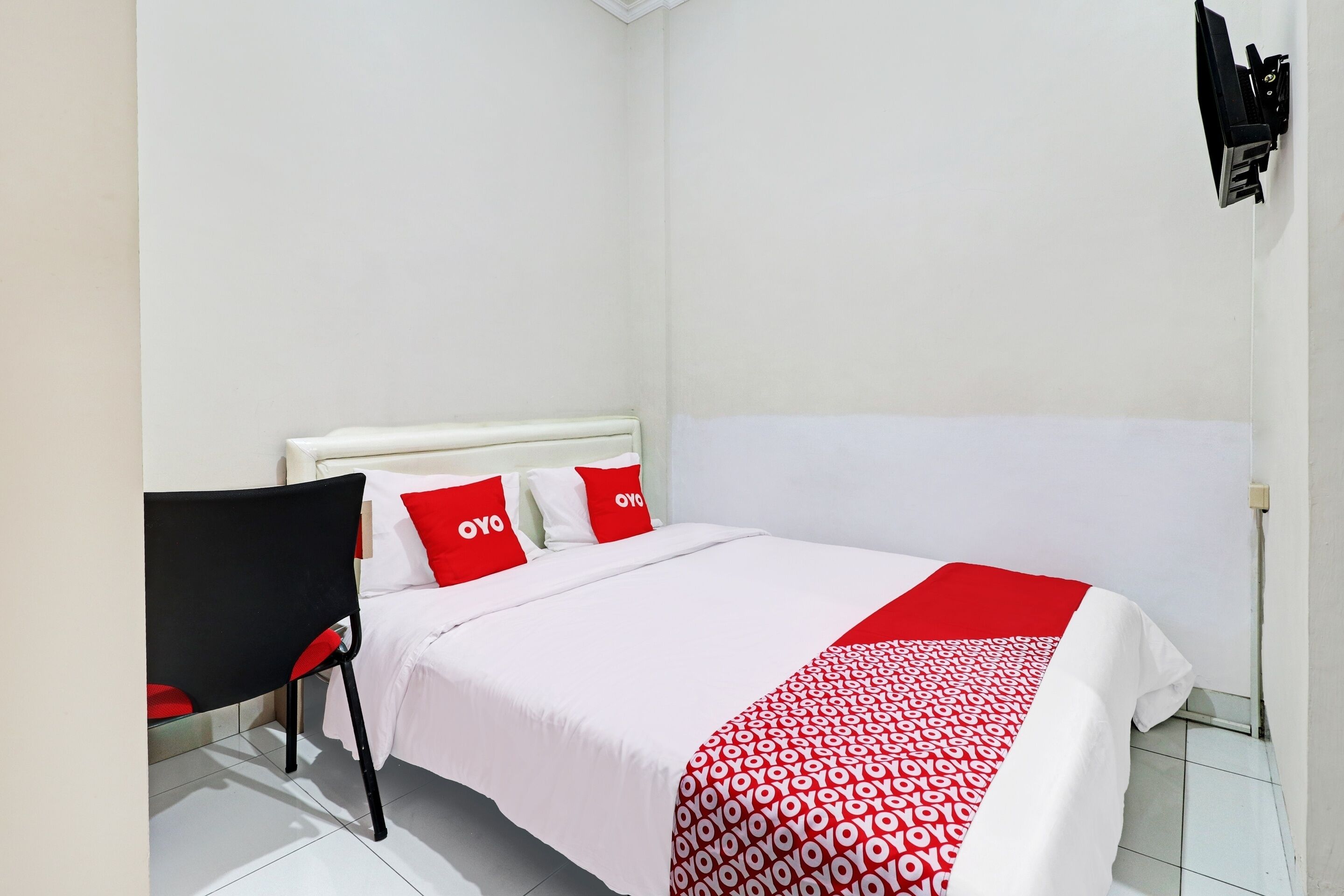 Un dormitorio con una cama, una silla y un televisor instalado en la pared.