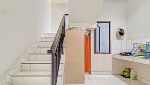 A staircase leading to an upper floor, a door with a cardboard box, a gas cylinder, and a shelf with various items. - OYO 90452 Pillow Inn (Karawang)
