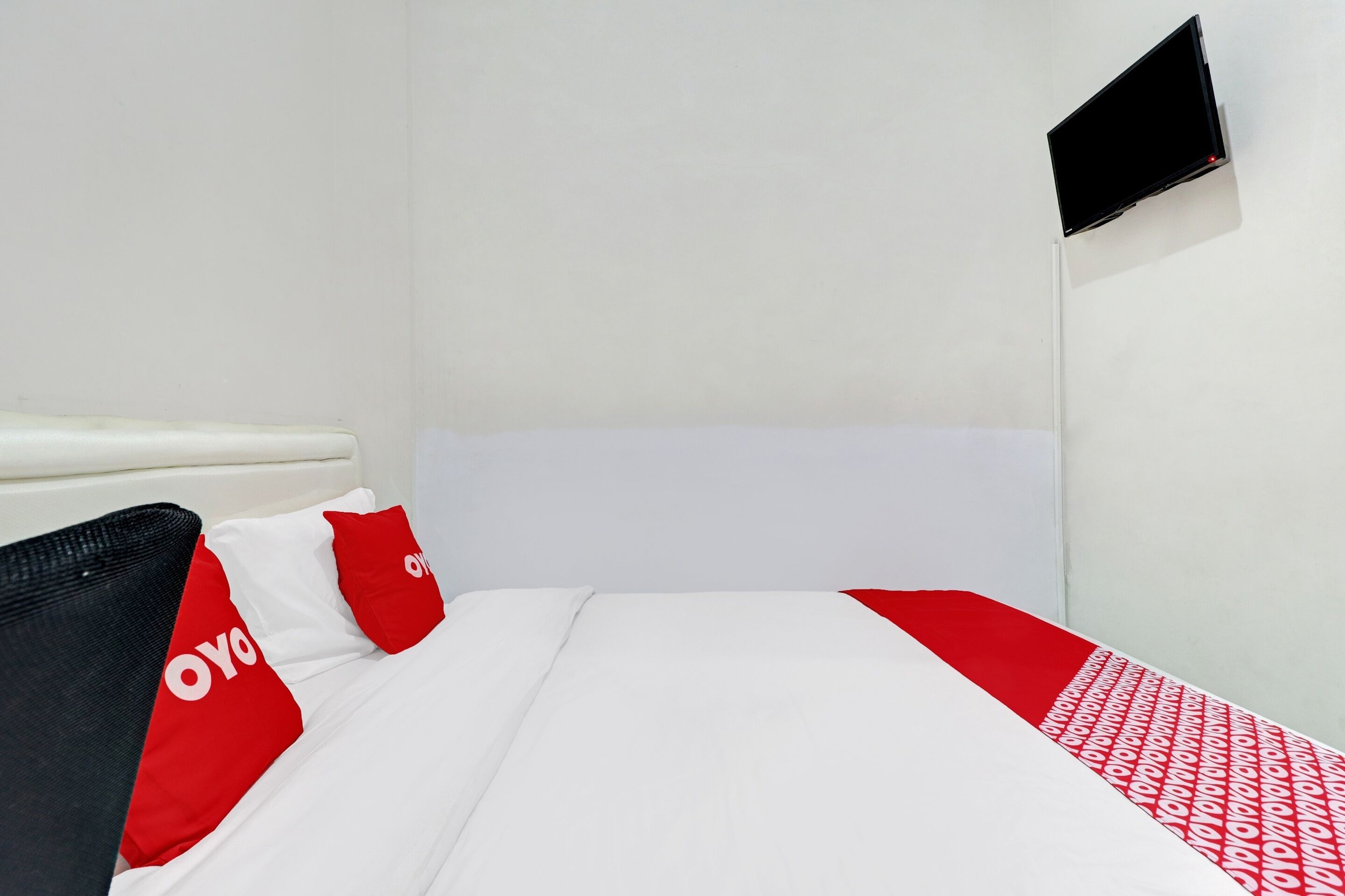A hotel room with a bed, a TV mounted on the wall, and a red and white patterned bedspread.
