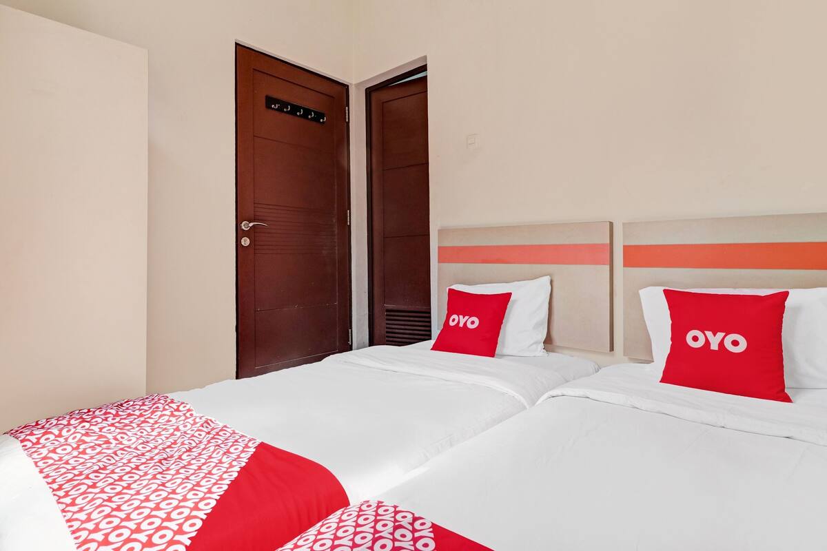 A hotel room with two beds, each with a red pillow labeled "OYO".