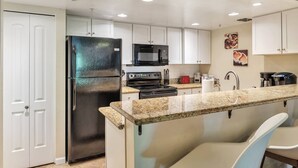 A modern kitchen with white cabinets, a stainless steel refrigerator, a microwave, a stove, and a granite countertop. - Fantastic Location! Heated Pool, Close to Giants Stadium, Minutes from Old Town Scottsdale + Golfing (Scottsdale)