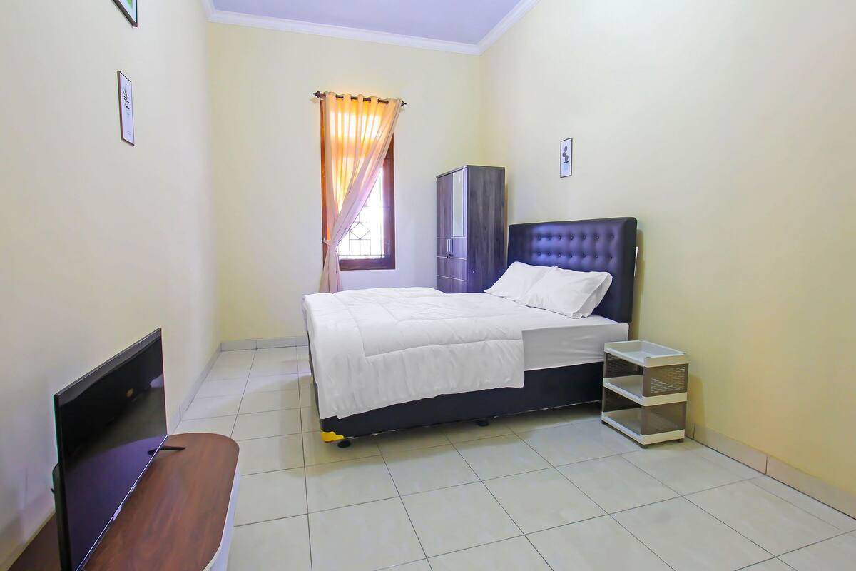 A bedroom with a bed, a wardrobe, a bedside table, and a window with curtains.