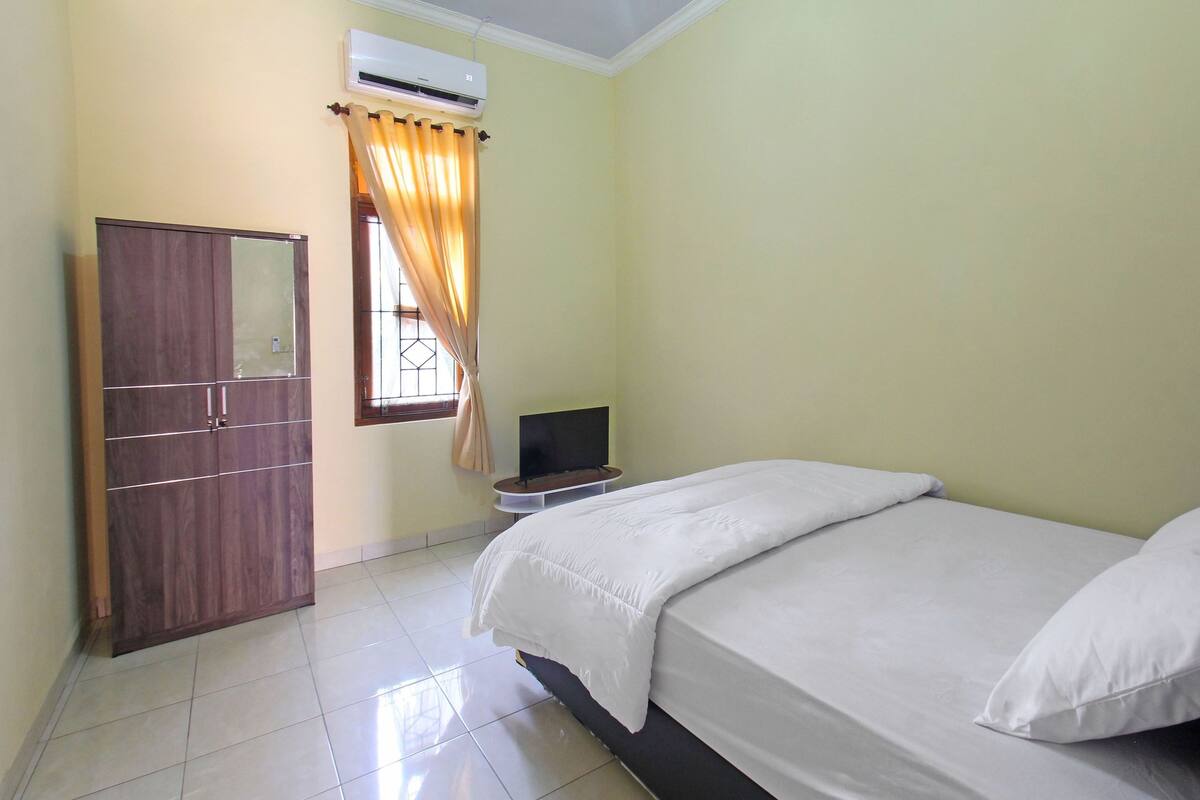 A bedroom with a bed, a wardrobe, a television, and an air conditioning unit.