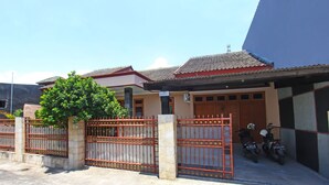 A gated residential area with a paved driveway, a tree, and two motorcycles parked near a building with a tiled roof. - OYO 91777 Kemuning Guesthouse (Sempe)
