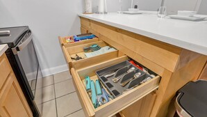 Una cocina con encimera de madera, un cajón con utensilios de cocina y un reloj en la pared.