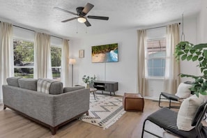 A living room with a grey sofa, a small table, a TV, and a ceiling fan.
