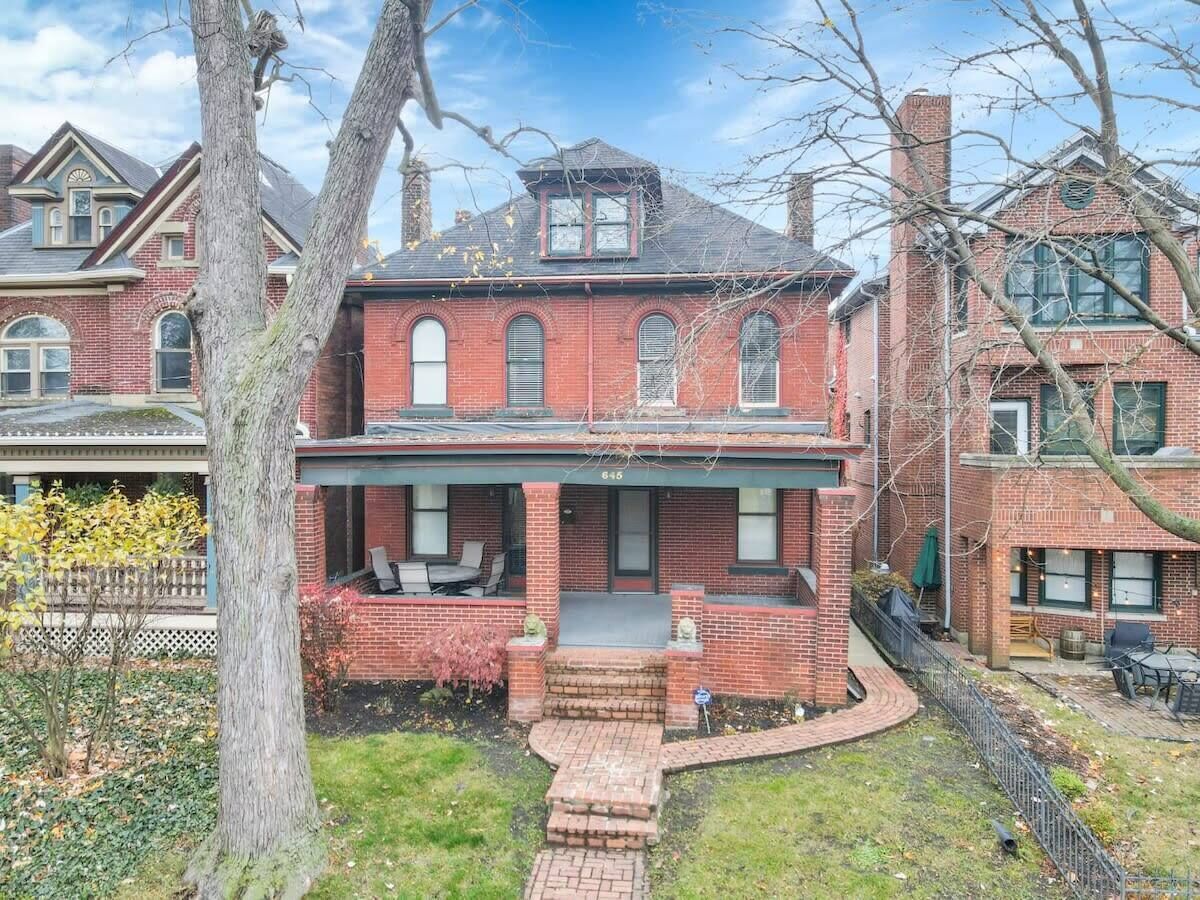A two-story brick house with a front porch, a small front yard, and a visible number '645' on the front.