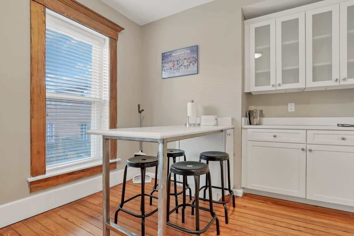A kitchen with white cabinets, a white countertop, and three black stools.