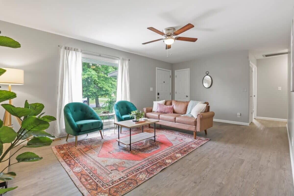 Un salon doté d’un ventilateur de plafond, de deux fauteuils, d’un canapé, d’une table basse et d’un grand tapis.